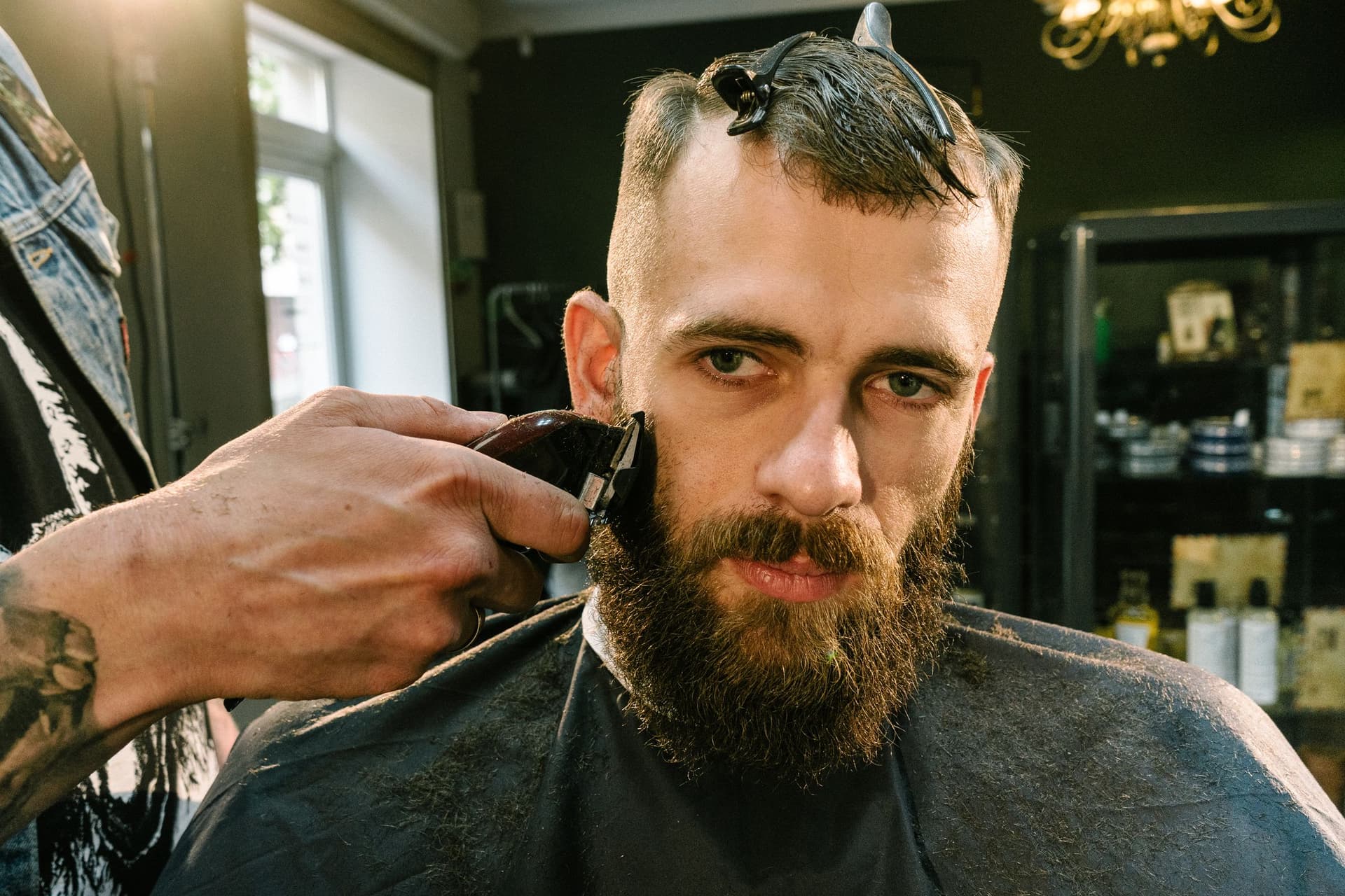 Barber trimming a client's beard with clippers in a barbershop