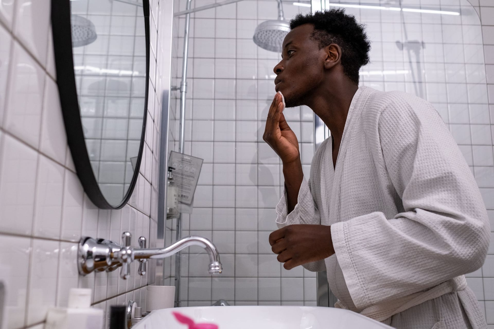 Man in a bathrobe applying a skincare routine at the bathroom mirror
